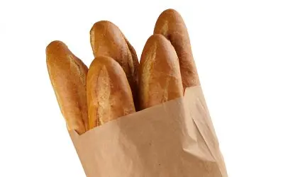 Four baguettes are partially visible inside a brown paper bag, isolated on a white background.